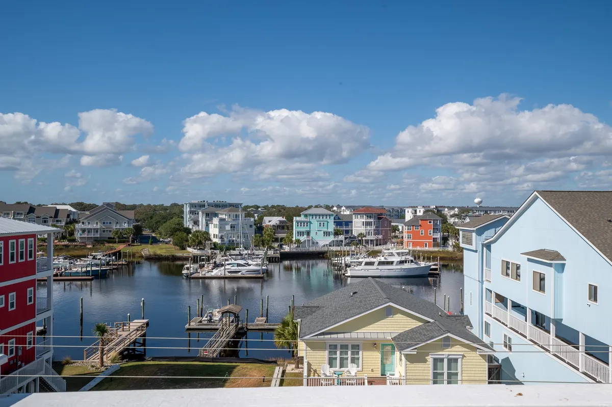 A cheerful waterfront scene featuring colorful houses, boats docked along the water, and a vibrant sky. The setting conveys a lively, coastal community vibe and proximity to boating or marina activities.