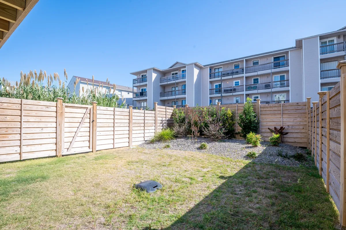 A peaceful and private fenced yard with lush vegetation, surrounded by secure fencing and adjacent to apartment buildings. The space is open and inviting, perfect for kids and pets to play safely while parents relax nearby. The fencing ensures privacy and security, central to the section's focus.