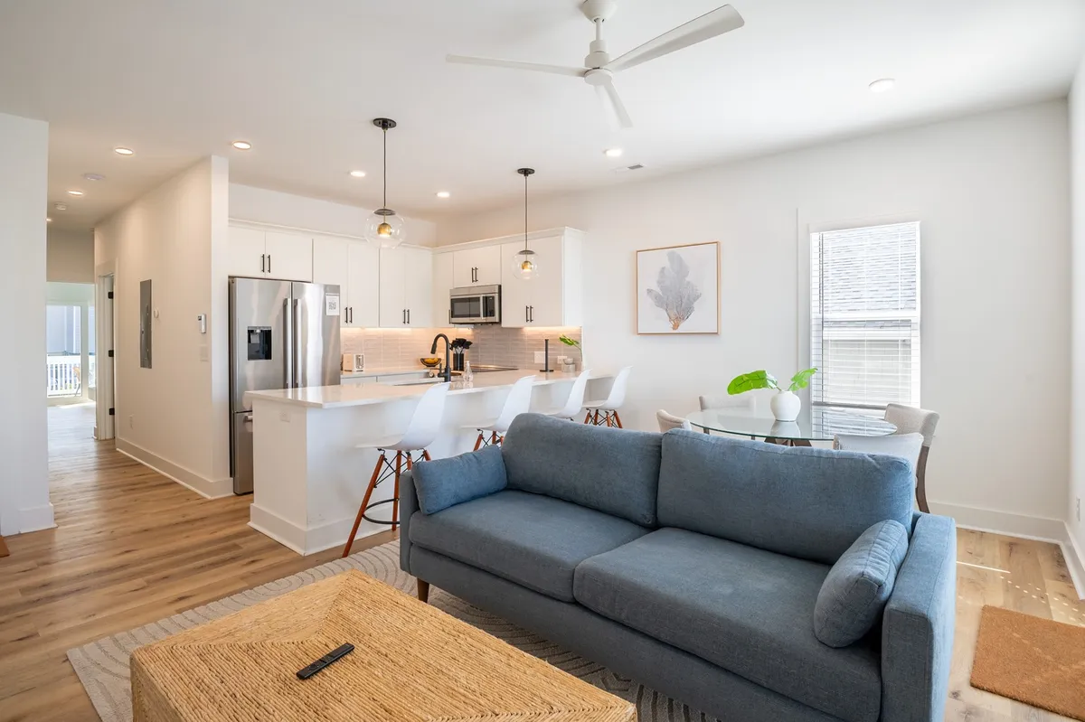 A welcoming interior with a blue sofa, a kitchen island, a dining area with a table and chairs, and vibrant artwork on the wall. The setting feels inviting and perfect for both casual and special occasions.