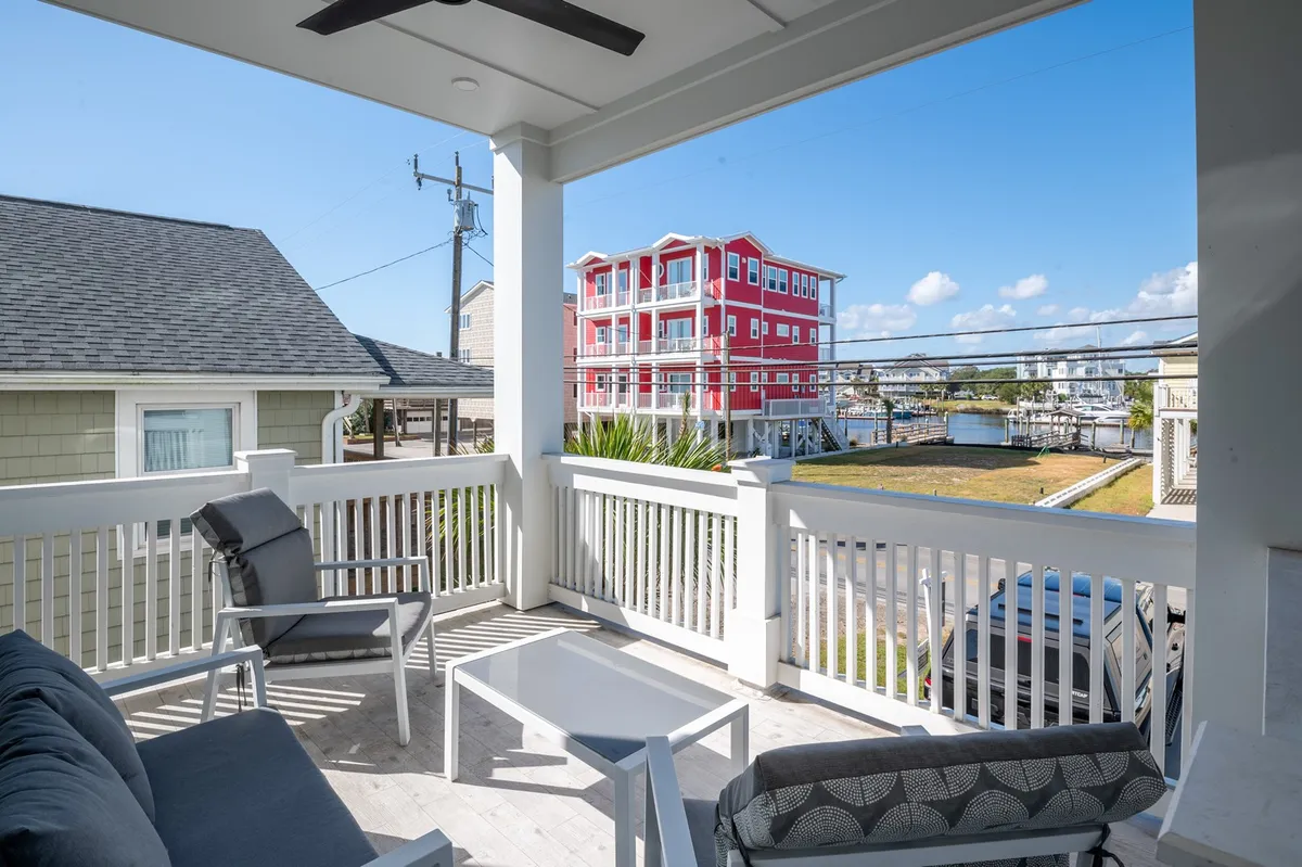 An inviting outdoor seating area beside a bright red building, looking out over the water. The ambiance suggests a perfect spot for sunset watching, evening barbecues, and relaxed socializing with friends.