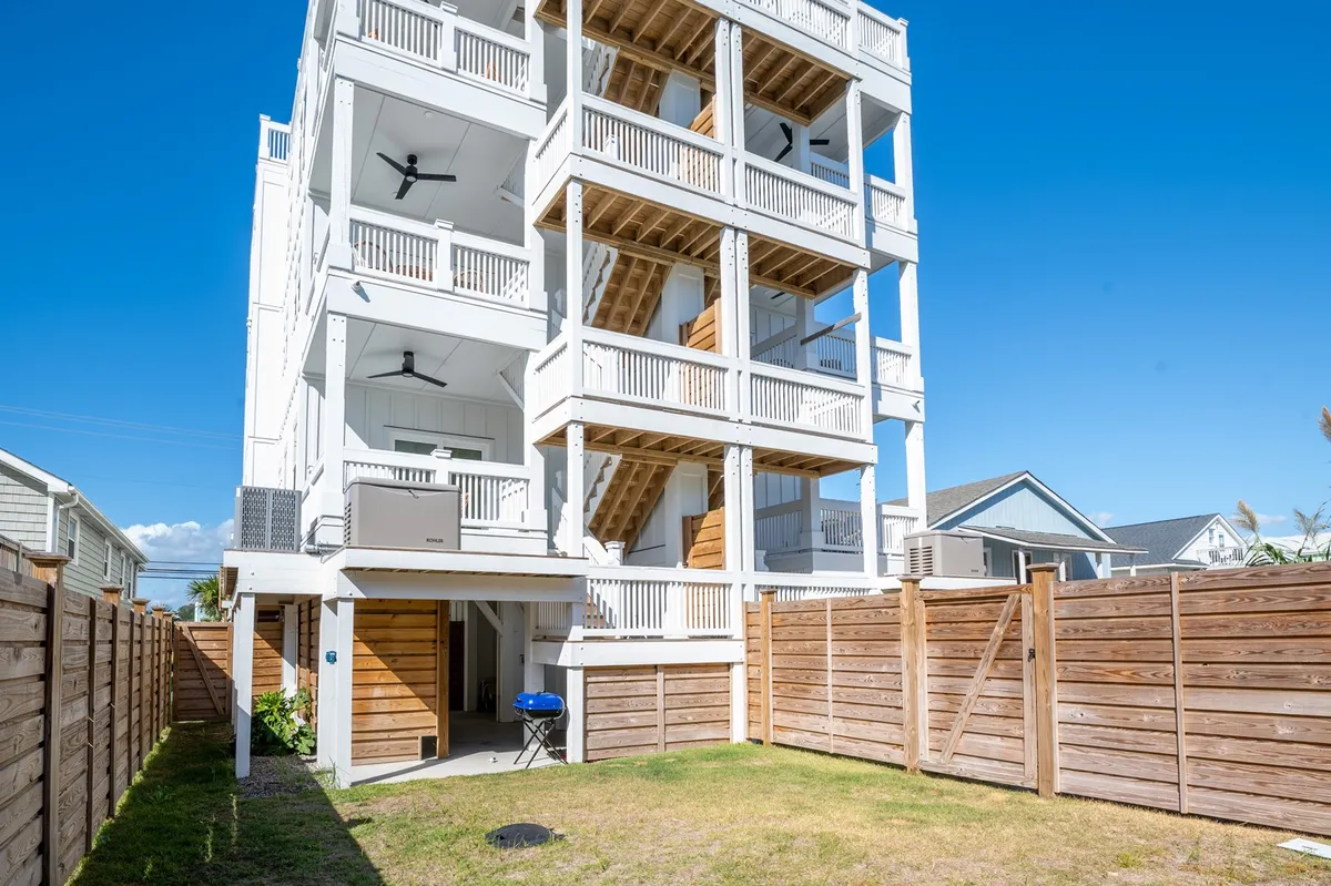 A multi-level exterior structure with a large wooden fenced yard, lawn, and an outdoor grill. The image captures sunny spaces for barbecuing and relaxing, balconies for morning coffee, and ample yard space for gatherings and play. The wooden fence provides privacy and safety, and the outdoor grill area adds to the functionality for families and groups.