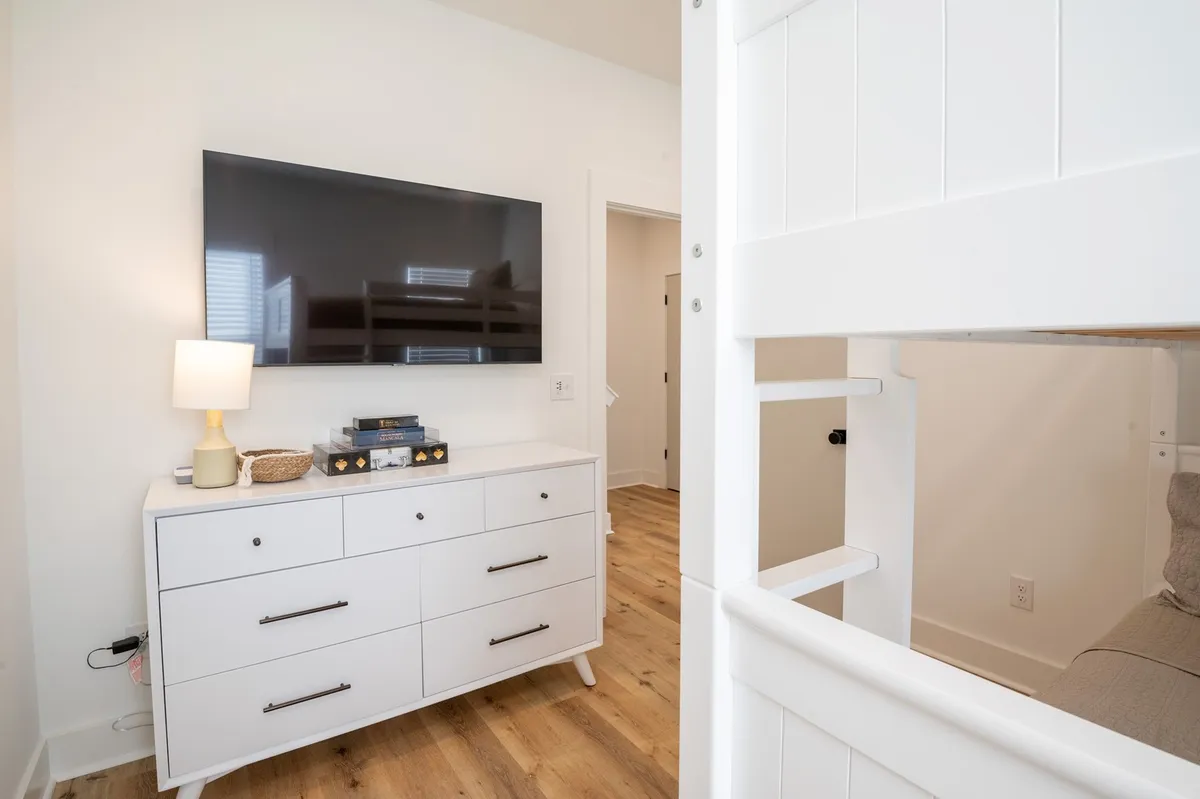 A welcoming bunkroom showcasing a sturdy bunk bed, a dresser, and a wall-mounted TV. The room is designed for relaxation and play, with enough space for children or groups to unwind and enjoy bedtime movies or games.