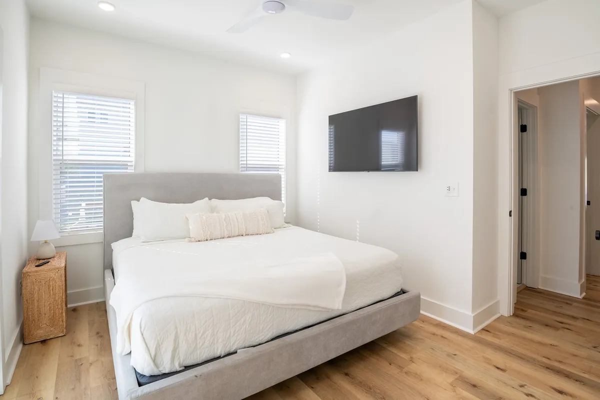 A serene king suite featuring a comfortable bed with soft linens, a nightstand, and a wall-mounted TV. Natural light streams in through windows, creating a peaceful and inviting atmosphere ideal for relaxation and privacy.