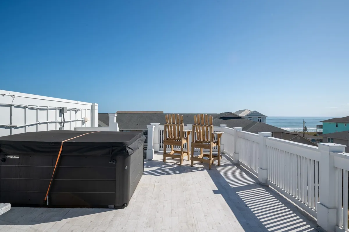 A serene rooftop scene featuring a hot tub surrounded by Adirondack chairs, all overlooking a stunning ocean view. The mood is tranquil, inviting guests to relax, socialize, and enjoy the sunset or starry skies.