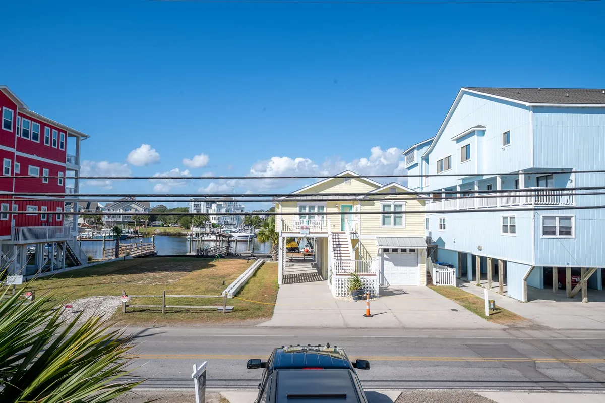 A cheerful waterfront scene featuring colorful houses, a marina dotted with boats, palm trees, and blue skies. The lively area hints at the boardwalk and local attractions a short walk away.