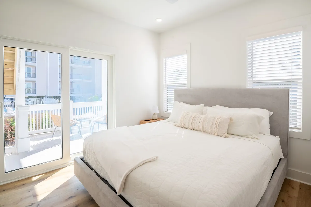 A tranquil king suite with a large bed, decorative pillows, and sliding glass doors that open to a private porch or balcony. The room is filled with natural light, offering a peaceful retreat and easy access to outdoor relaxation.
